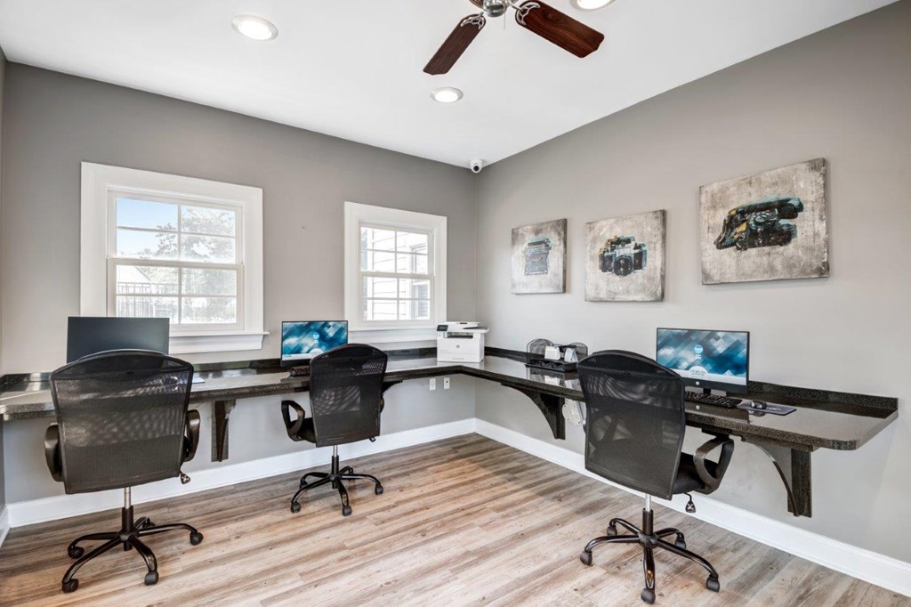 A room with a long table and chairs, a laptop on the table, and a ceiling fan.