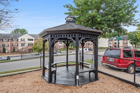 A gazebo with a black roof and a red car parked behind it.