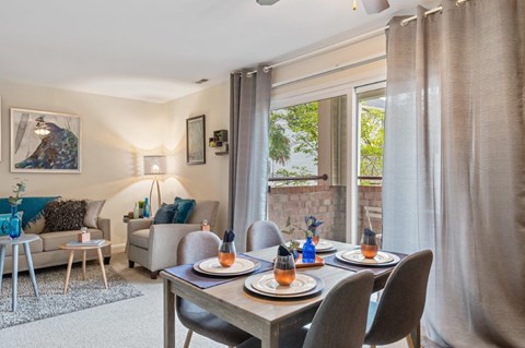 A dining room with a table set for two and a view of a garden outside.