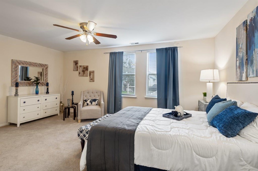 A bedroom with a large bed, a dresser, a mirror, and a ceiling fan.