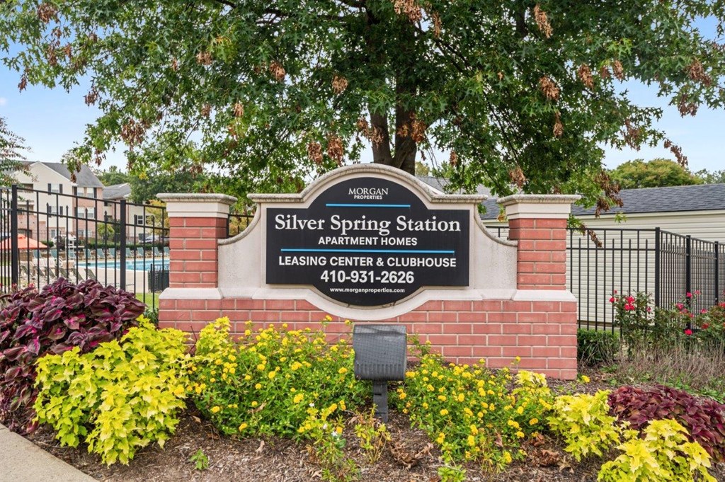 A sign for Silver Spring Station leasing center and clubhouse is surrounded by flowers.