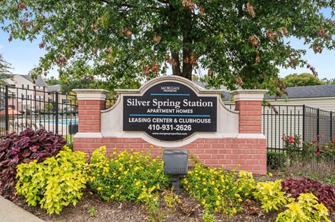 A sign for Silver Spring Station leasing center and clubhouse is surrounded by flowers.