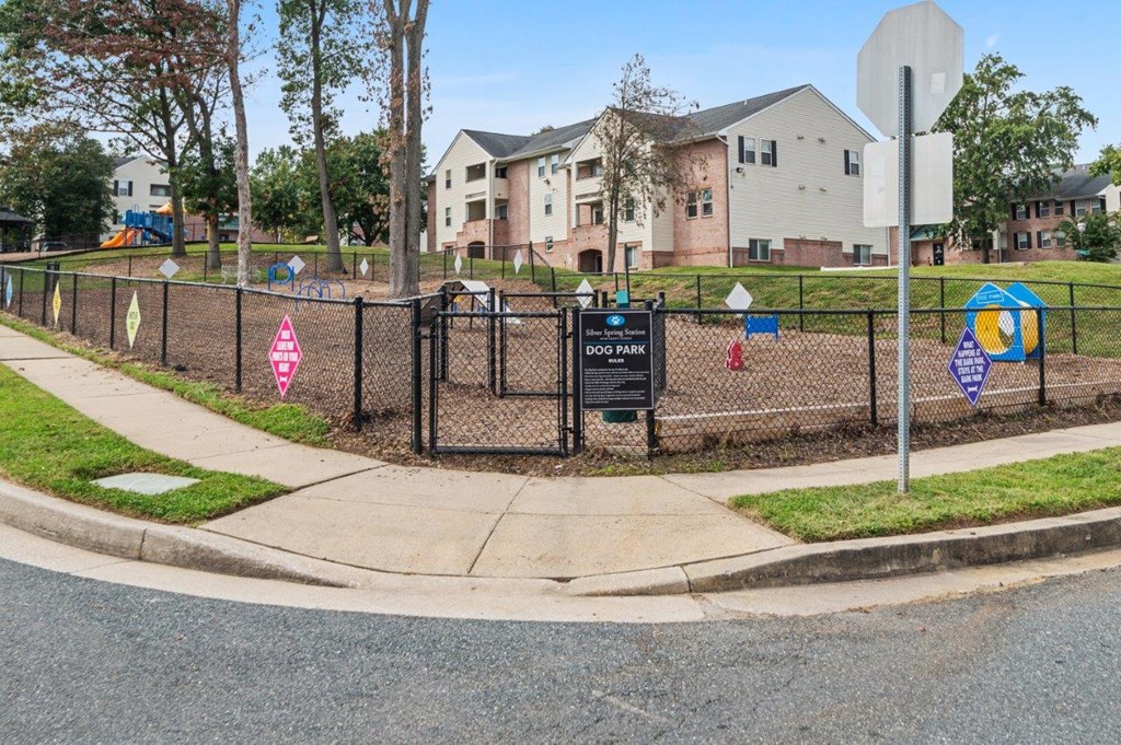 A dog park sign is posted on a fence in front of apartment buildings.