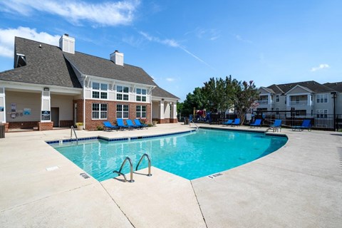 A swimming pool in front of a building with blue chairs around it.