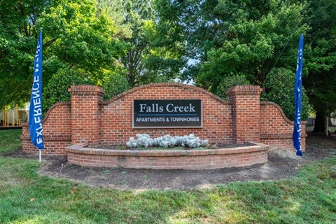 A sign for Falls Creek Apartments and Townhomes is surrounded by trees.