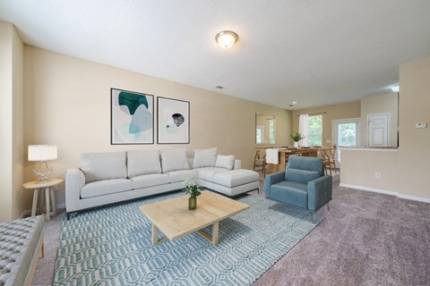 A living room with a grey sofa, a blue armchair, a wooden coffee table, and two abstract paintings on the wall.