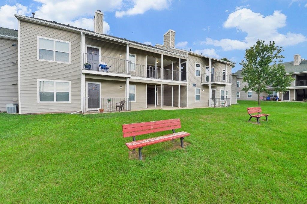 a bench in the grass in front of an apartment building