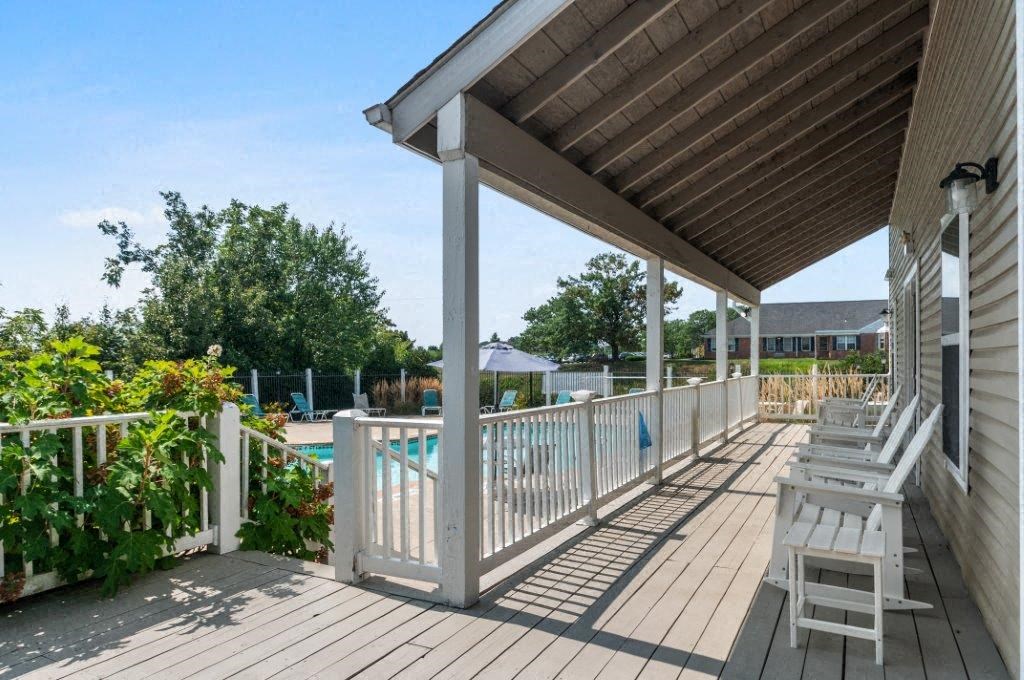 a covered porch with a pool and white deck chairs
