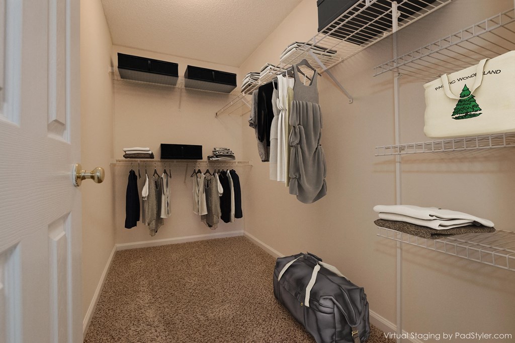 a walk in closet in a home with clothes hanging on racks and a luggage bag