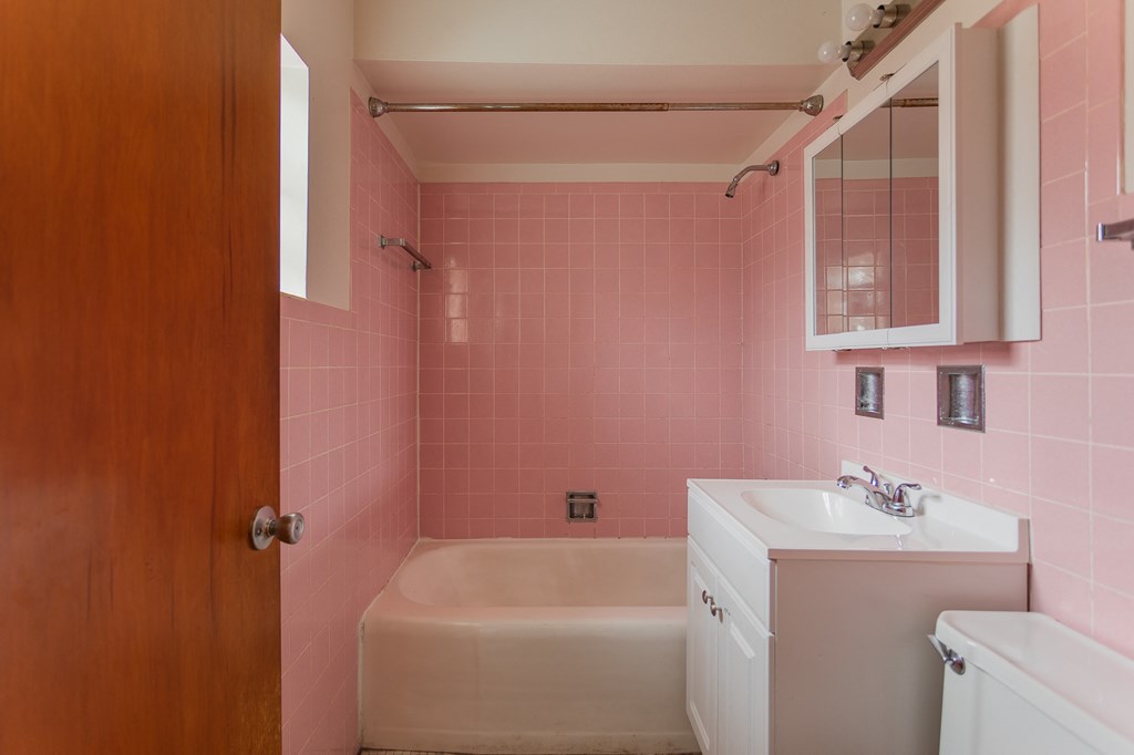 a bathroom with pink tiles and a white sink and a tub