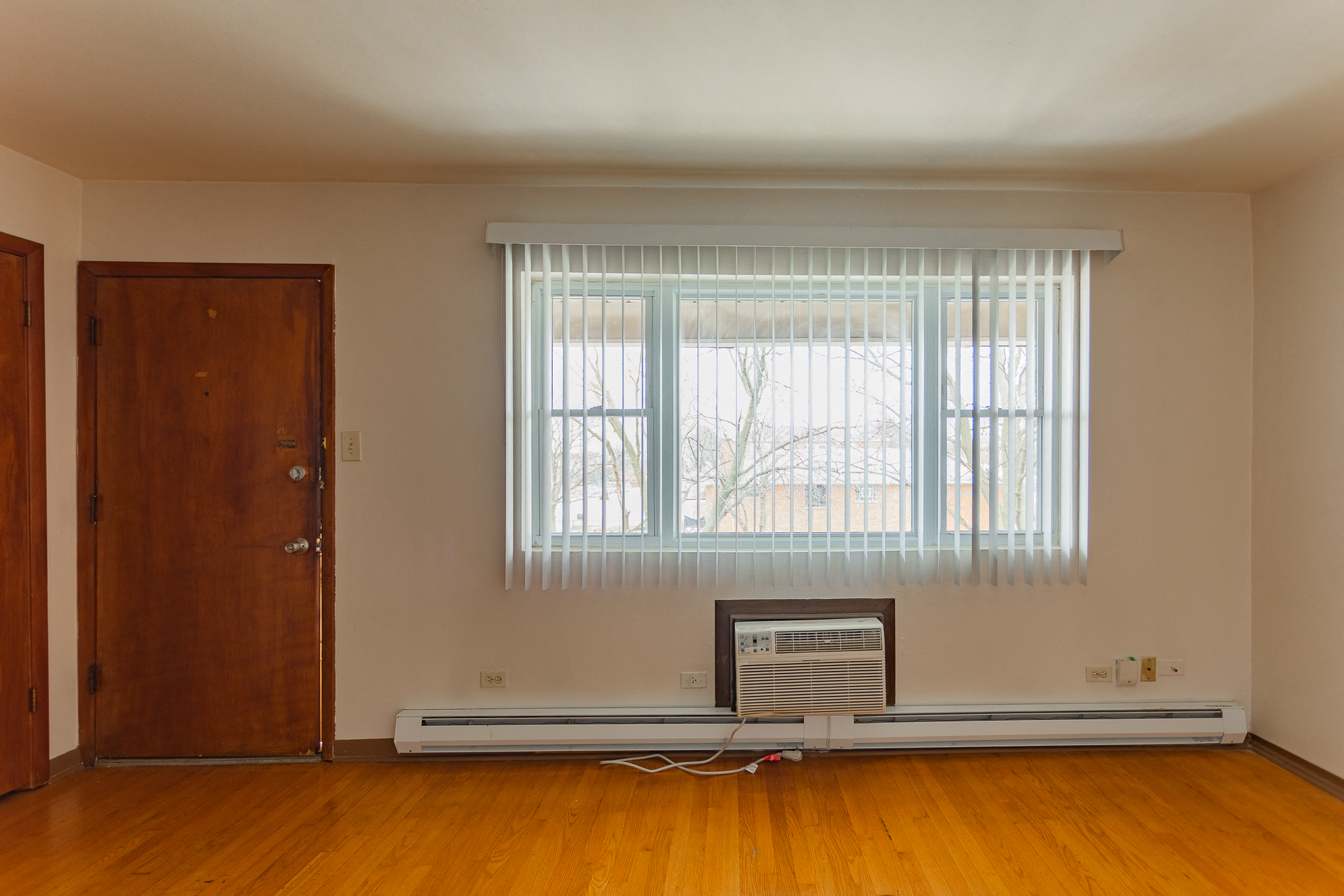 an empty living room with a window and a heater on the floor