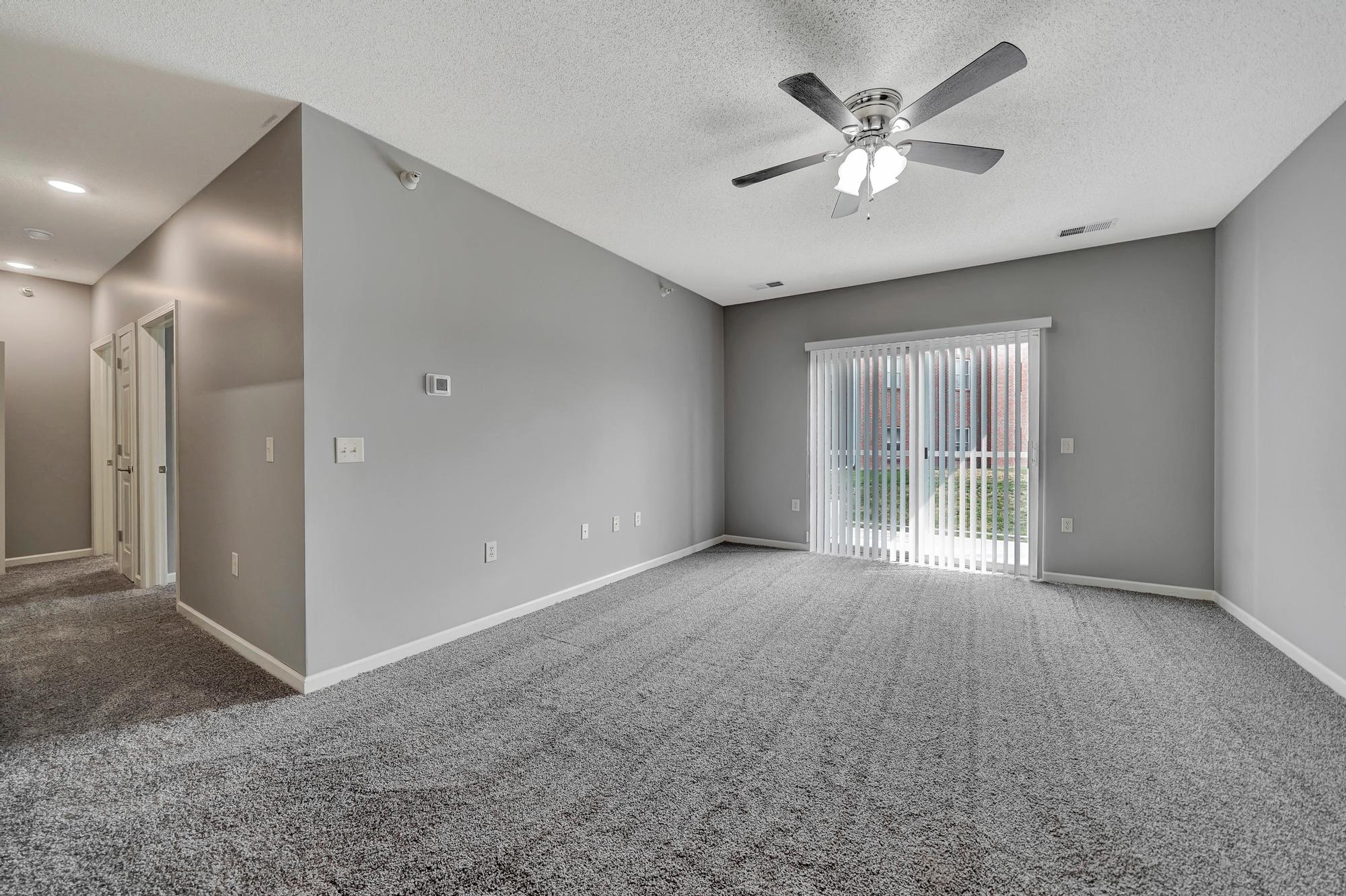 an empty living room with a ceiling fan and a window
