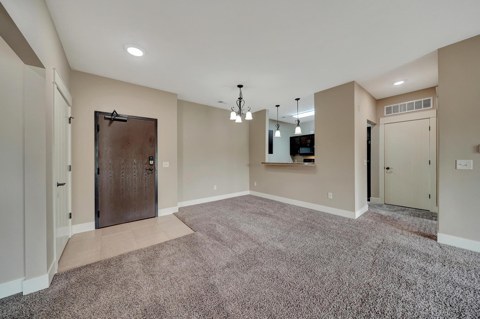 an empty living room with a door to the kitchen and a carpeted floor