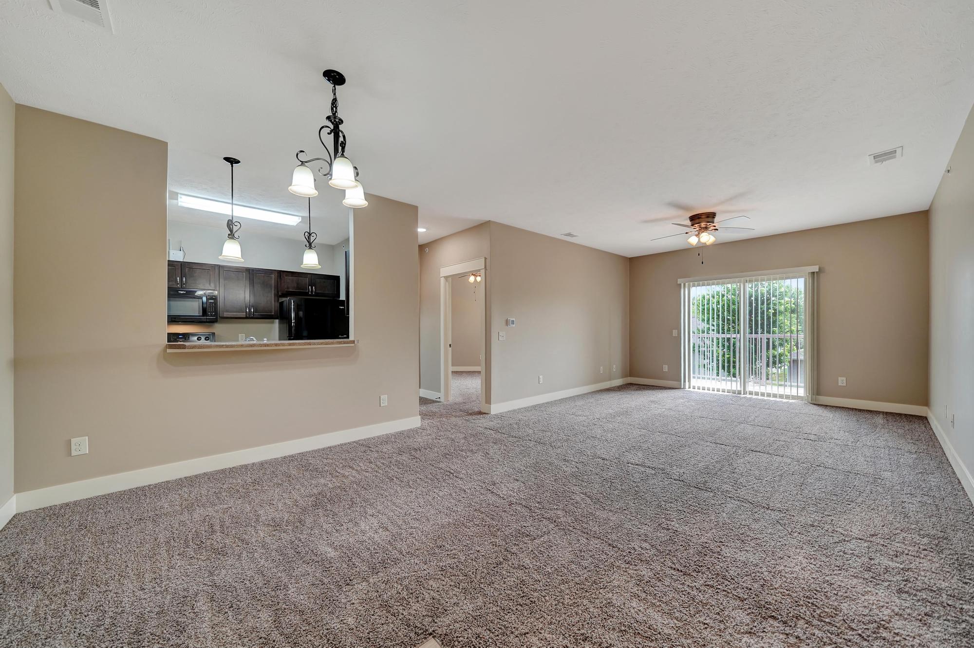the living room and dining room of a new home with carpet and a ceiling fan
