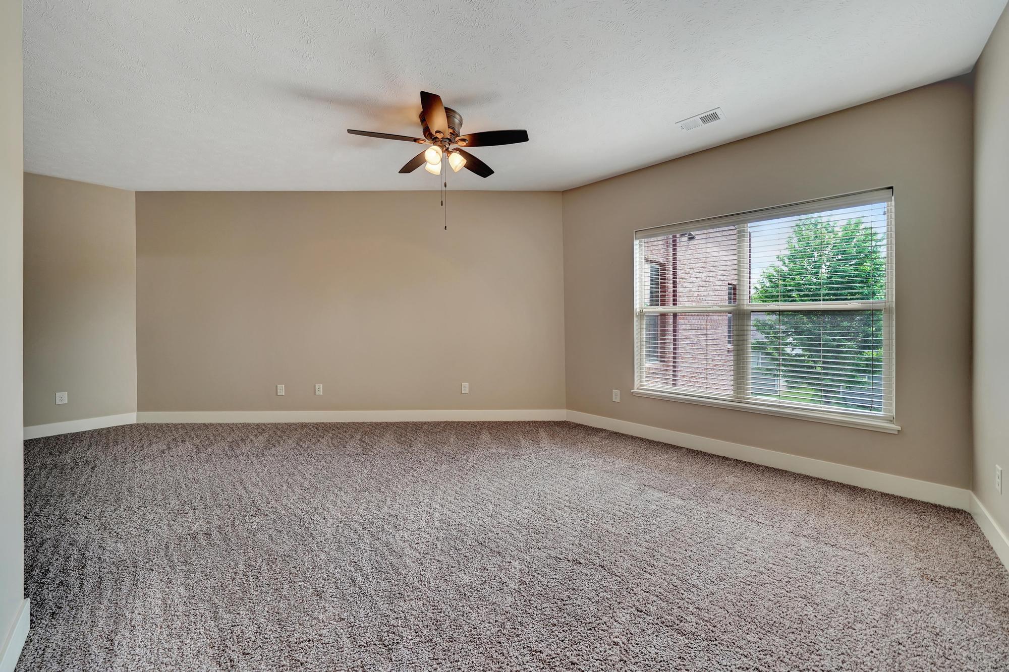 an empty living room with a large window and a ceiling fan