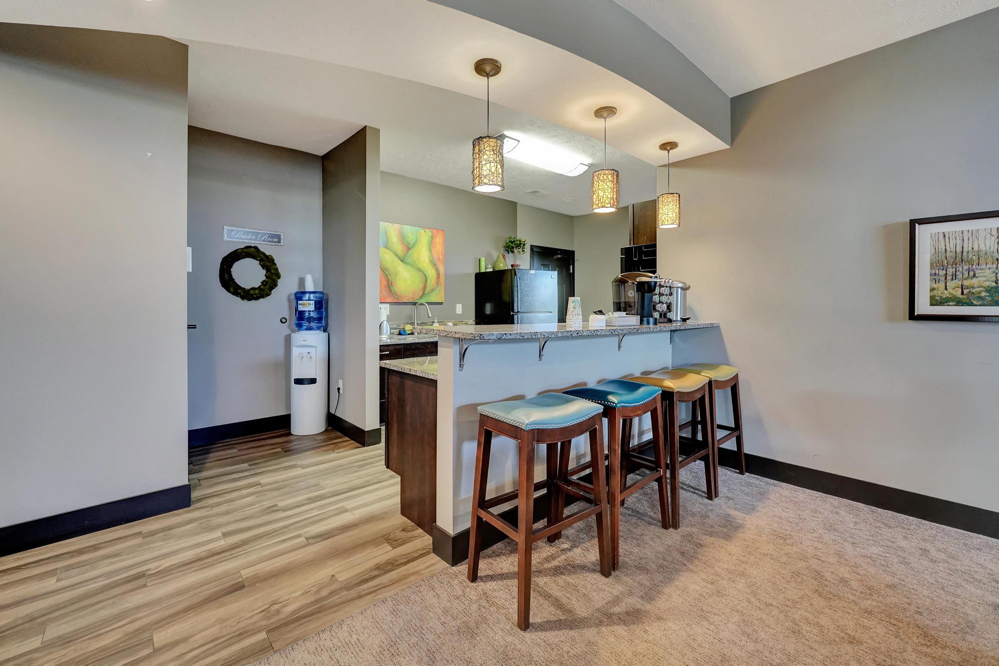 a bar with three stools in a living room with a refrigerator and a sink