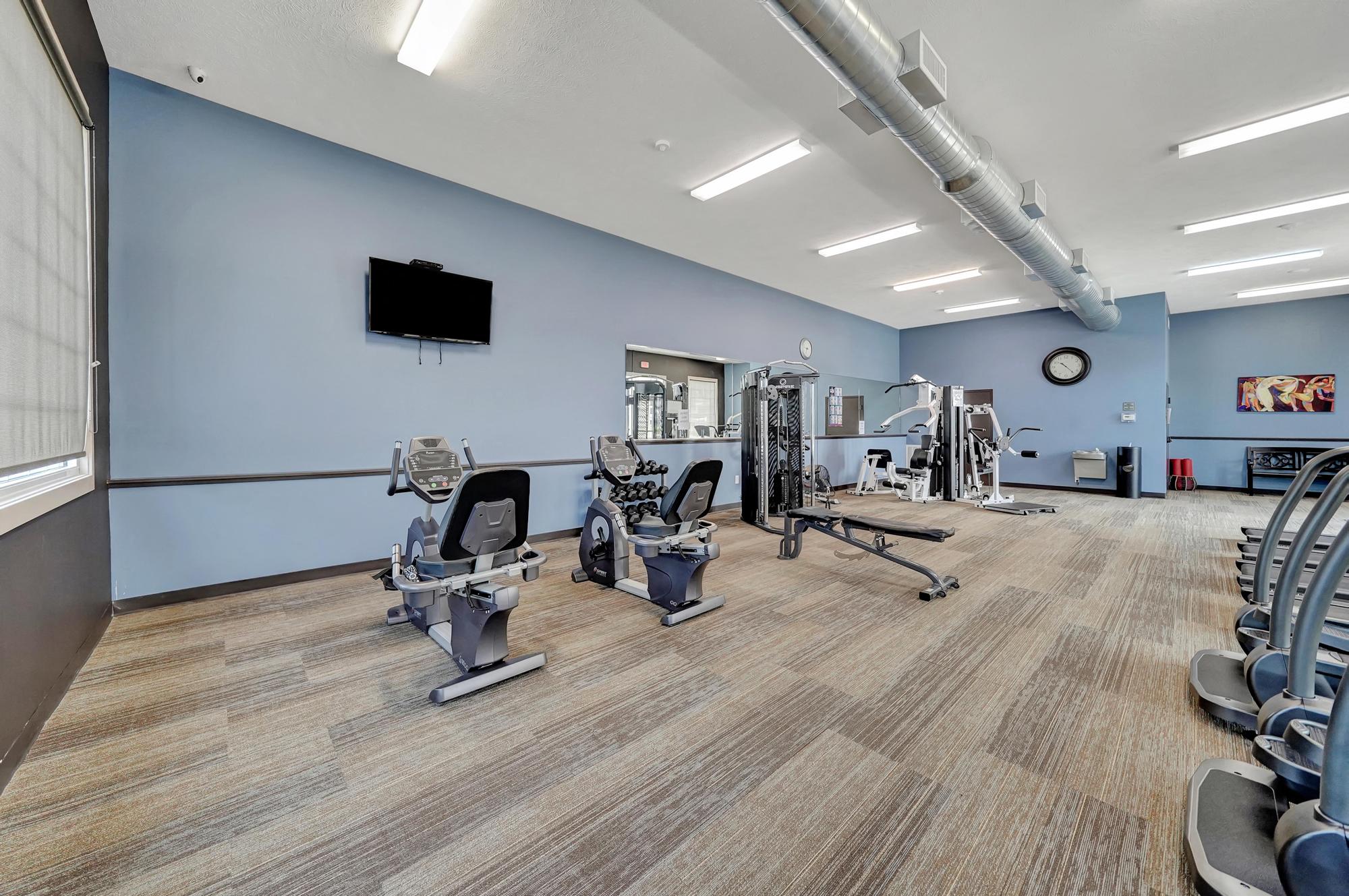 a gym with weights and cardio machines and a wall mounted tv