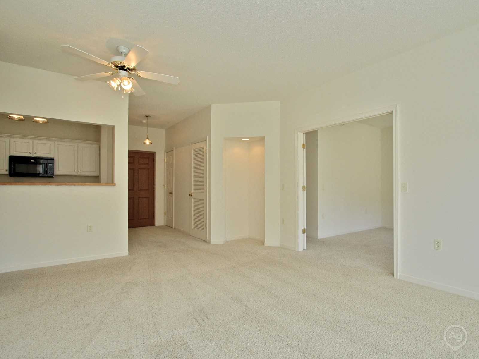 A spacious living room with a ceiling fan and carpeted floor.