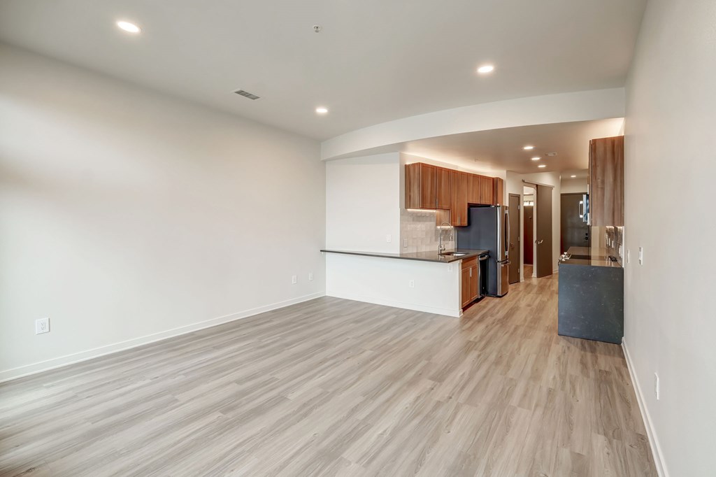 A room with wooden flooring and a kitchen area in the background.