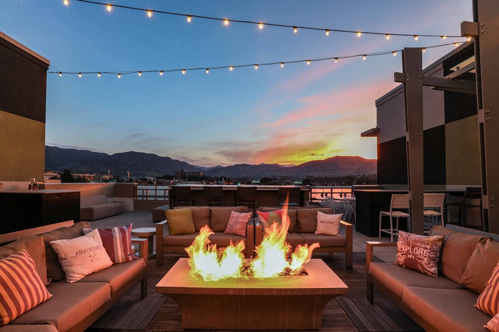 a fire pit on the rooftop of a building with couches and tables