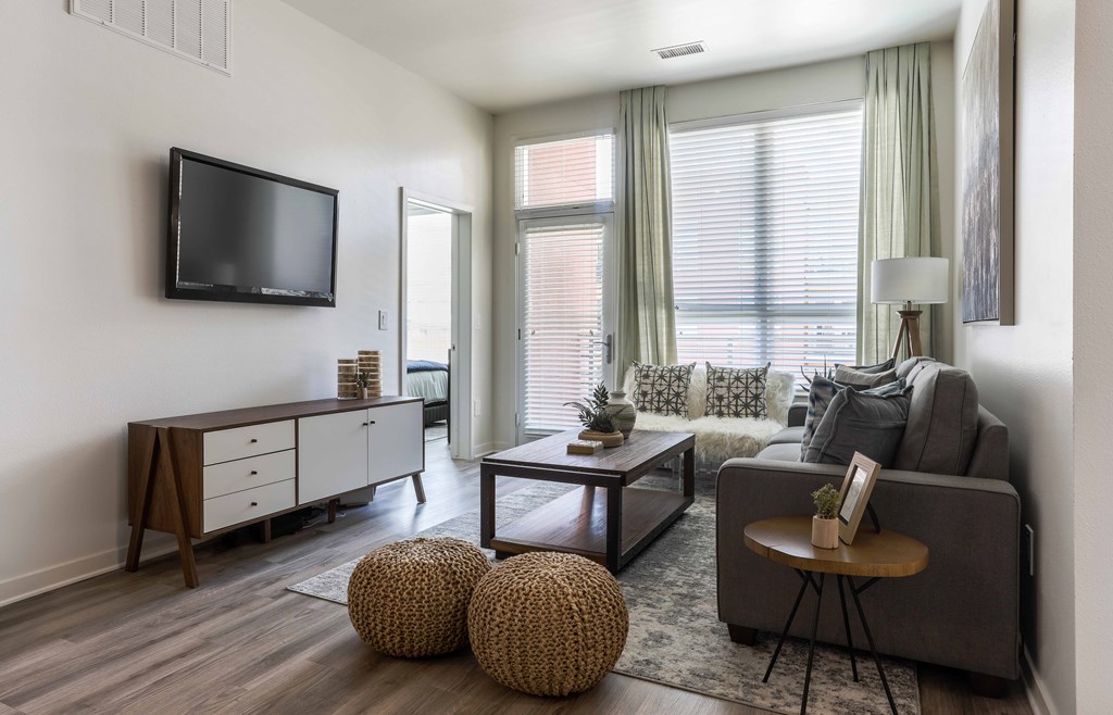A living room with a grey couch, a wooden coffee table, and a flat screen TV mounted on the wall.