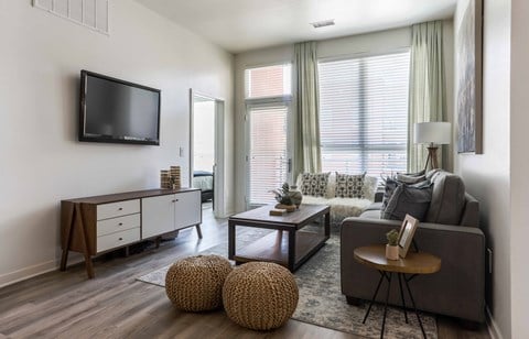 A living room with a grey couch, a wooden coffee table, and a flat screen TV mounted on the wall.