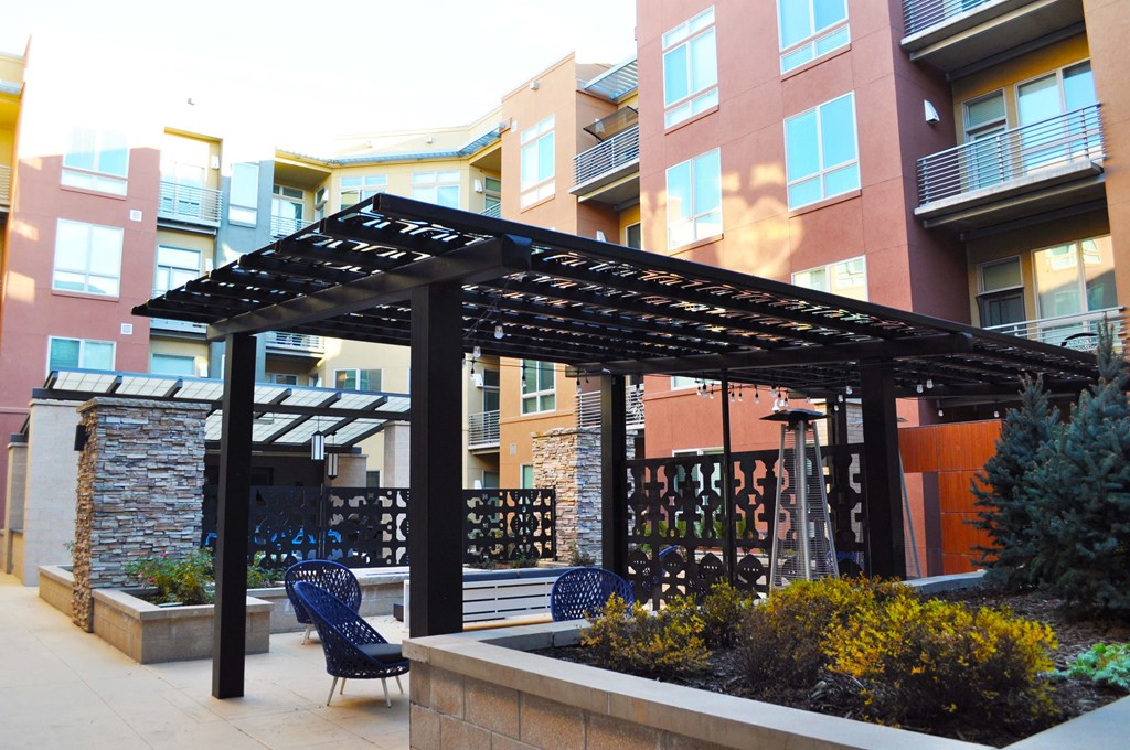 a patio with chairs and a pergola in front of an apartment building