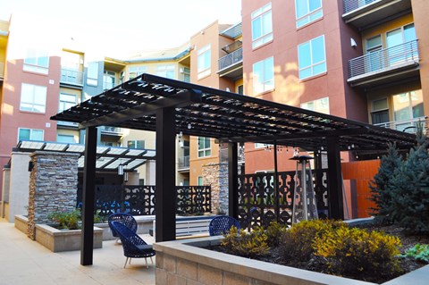 a patio with chairs and a pergola in front of an apartment building