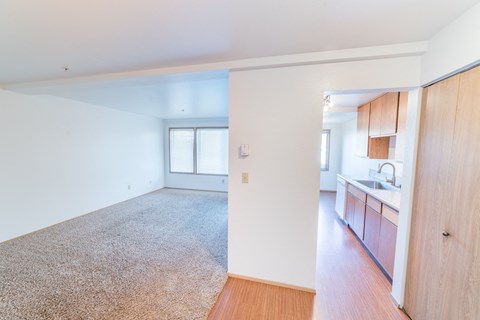 an empty living room and kitchen with wood floors and white walls