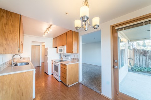 a kitchen with wooden cabinets and white appliances and a door to the living room
