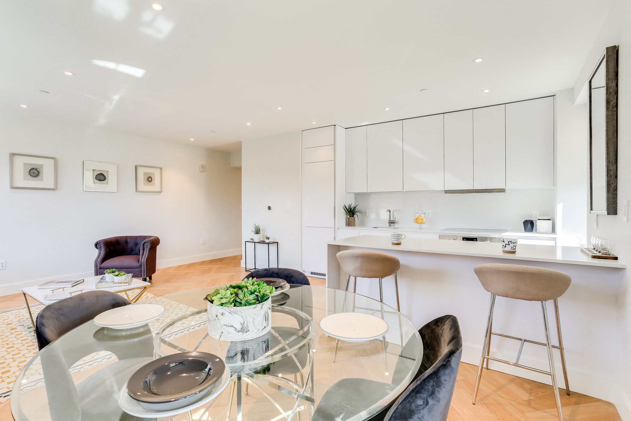 a living area with a glass table and a kitchen with white cabinets