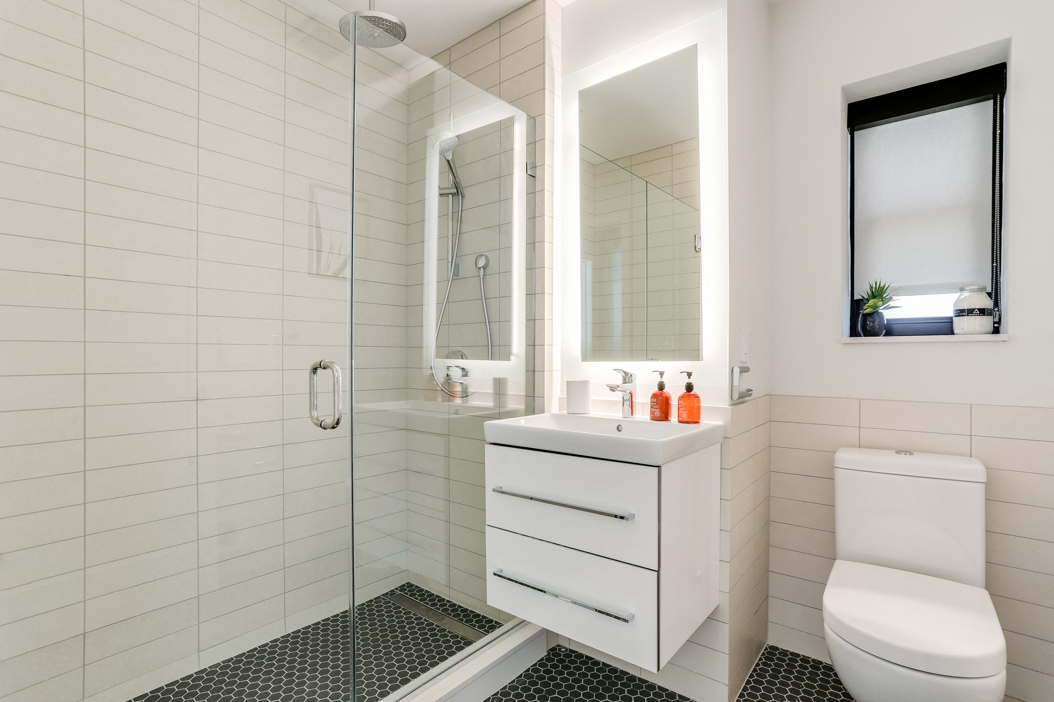 Bright tiled bathrooms with large backlit designer mirror, Hans Grohe chrome fixtures and Villeroy & Boch vanity