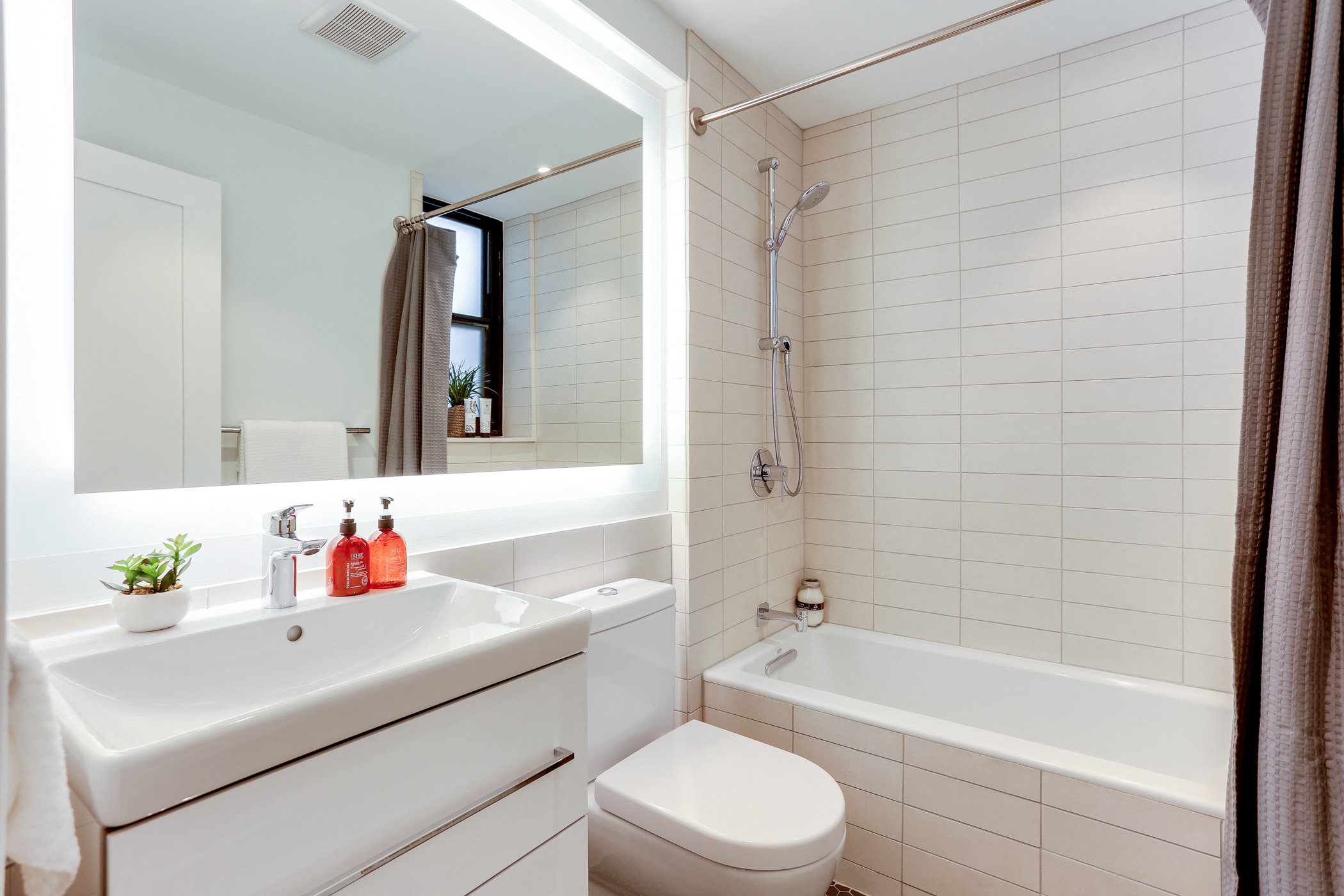 Bright tiled bathrooms with large backlit designer mirror, Hans Grohe chrome fixtures and Villeroy & Boch vanity