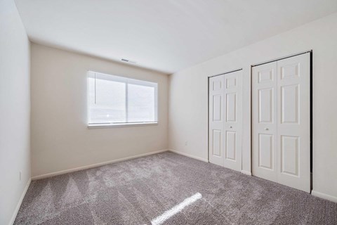 an empty bedroom with two doors and a window