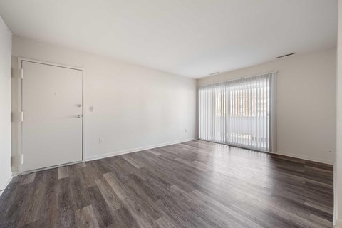 the living room of an apartment with wood flooring and a large window