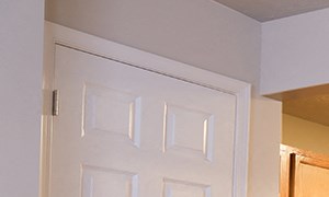 an empty living room with a kitchen with a black refrigerator