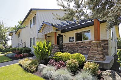 Exterior view of the leasing office with lush landscaping and an apartment building to the side in the background.