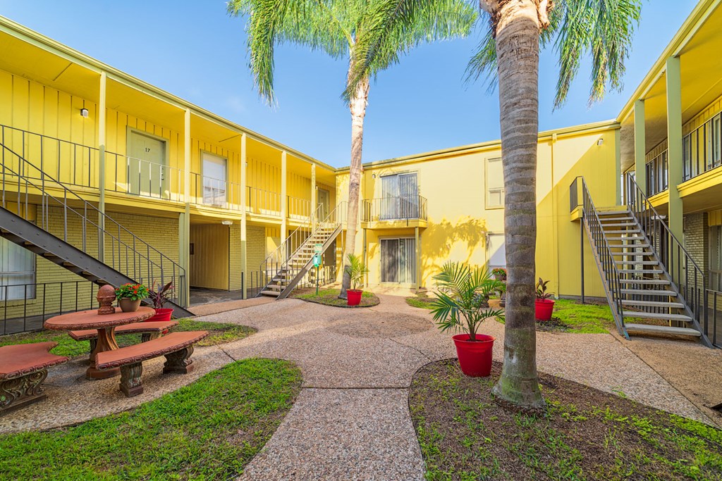 a courtyard with benches and palm trees in front of yellow buildings