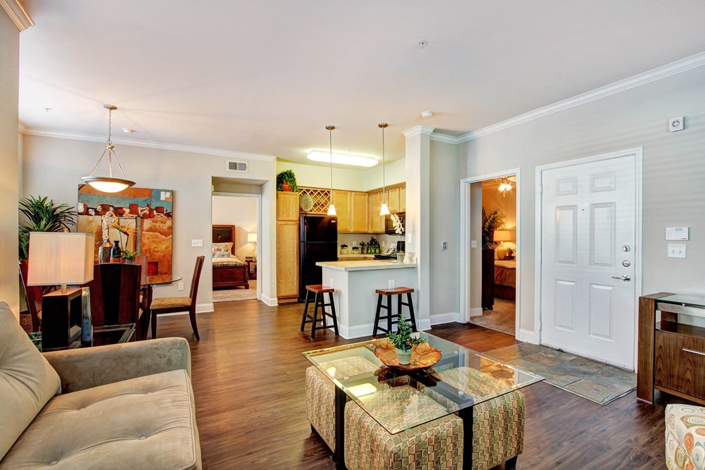 a living room with a couch and a glass coffee table in front of a kitchen