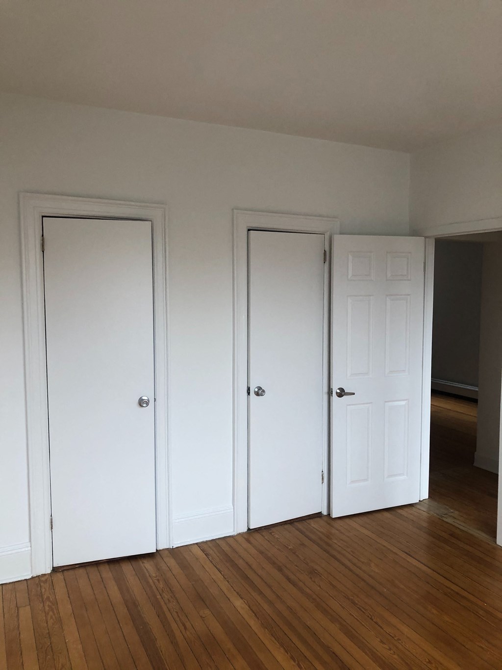 three doors in a room with wood floors and white walls