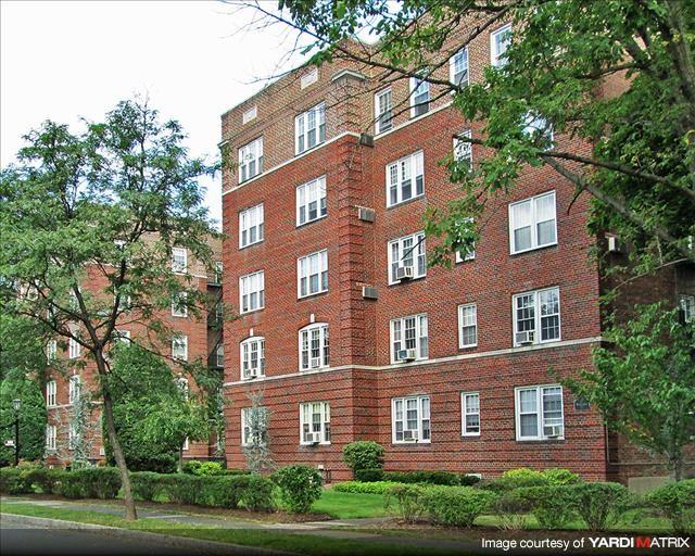 A red brick building with many windows and trees in front.