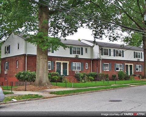 A white house with a red brick facade is surrounded by greenery.