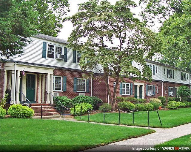 A white house with green shutters and a red brick front.
