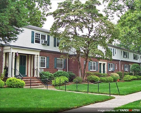 A white house with green shutters and a red brick front.