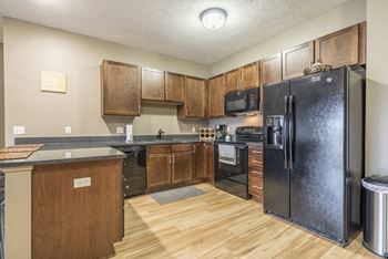 Kitchen with hard wood style floors, matching all black appliances, and brown finish cabinets at The Villas of Omaha at Butler Ridge in Omaha, NE