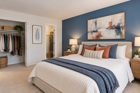 A bedroom with a large bed and a closet with clothes hanging.