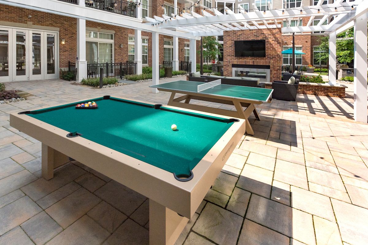a pool table in the patio of a building with two ping pong tables