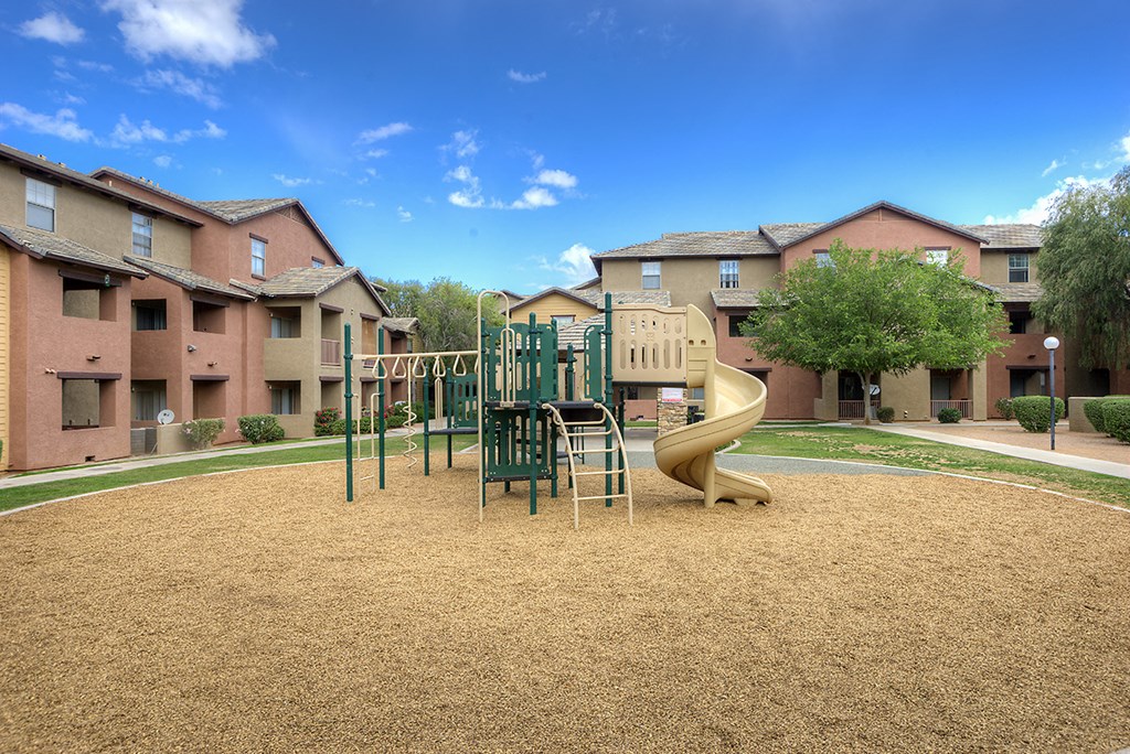 a playground with a slide and chairs in front of apartments