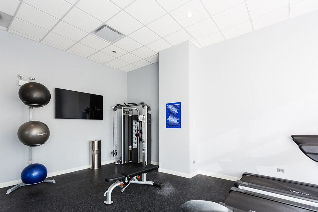 a gym with exercise equipment and a television in a white room