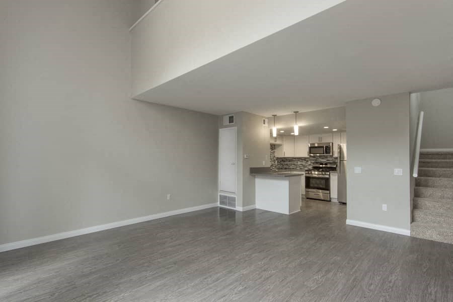 an empty living room with a kitchen in the background